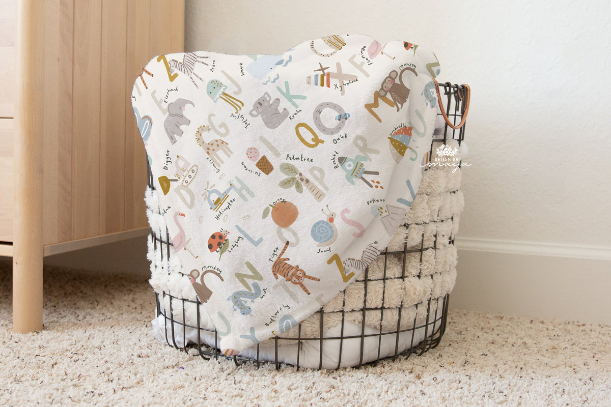 White alphabet blanket with pastel letters and animal illustrations, draped over a wire basket.