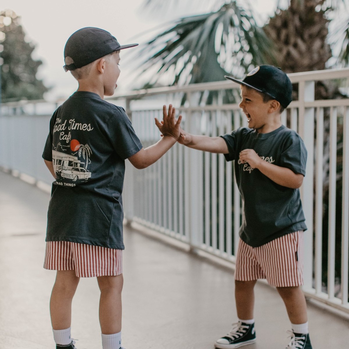 Two young boys standing outside giving each other a high five while wearing matching vintage graphic t-shirts.