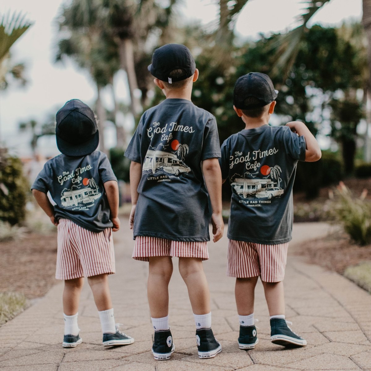 Three kids standing together outside wearing matching charcoal grey vintage graphic t-shirts.