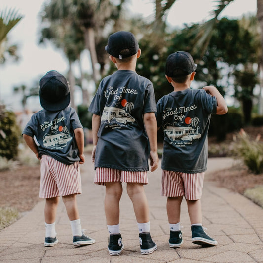 Three kids standing together outside wearing matching charcoal grey vintage graphic t-shirts.